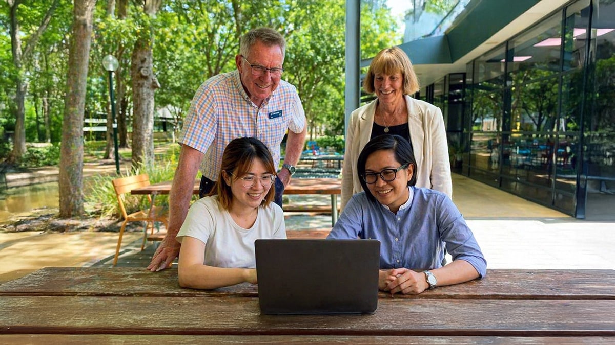 Group of university students collaborating outdoors at a campus table, discussing ideas on a laptop while working on a real-world innovation problem